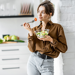 Portrait of a young and cheerful woman eating healthy salad on the kitchen at home