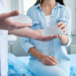 Doctor holding in his hands two silicone implants and female patient trying to touch them